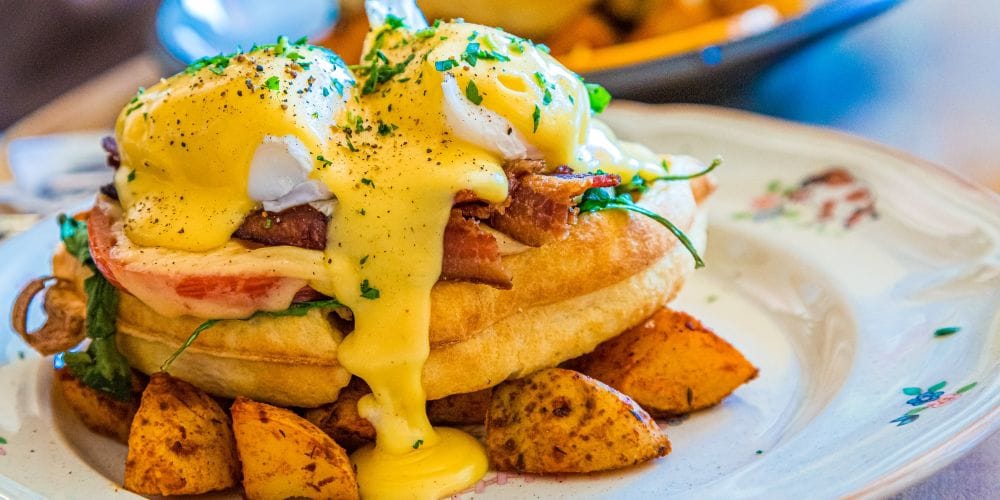 Ham and Bacon Benedict Served over Waffle and Potatoes